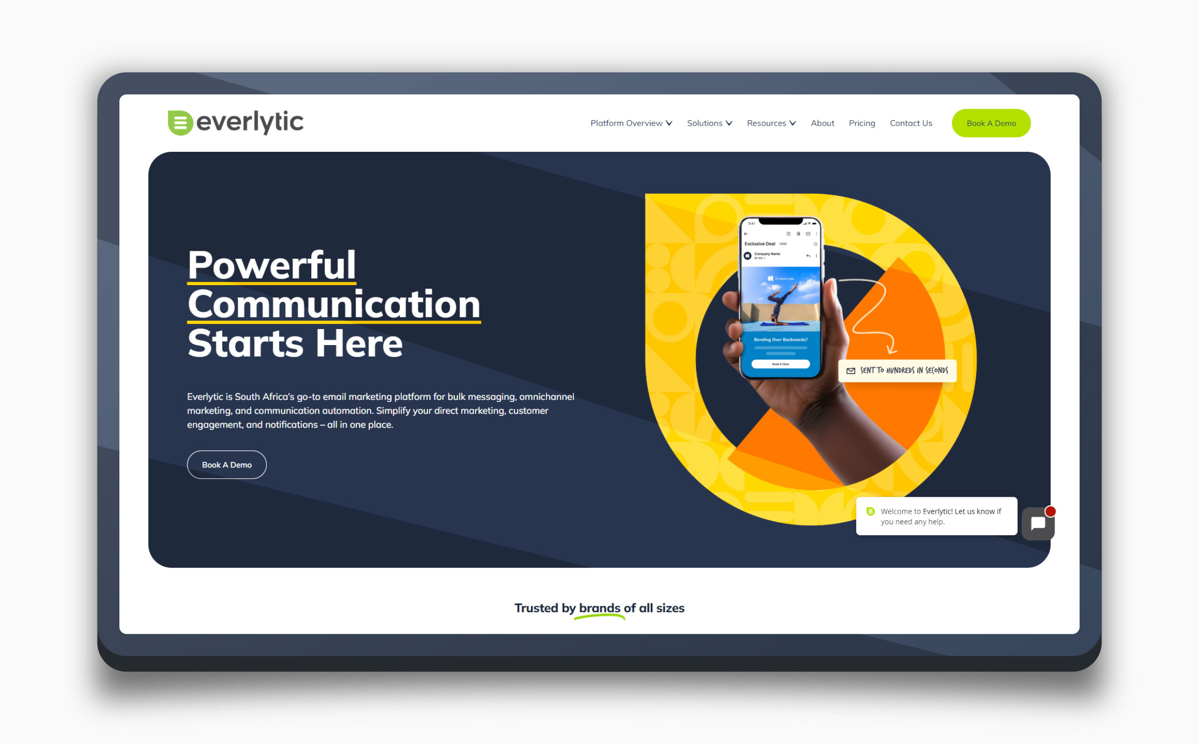 The current Everlytic website on a tablet — a dark navy hero reading "Powerful Communication Starts Here" with a hand holding a phone against a yellow graphic