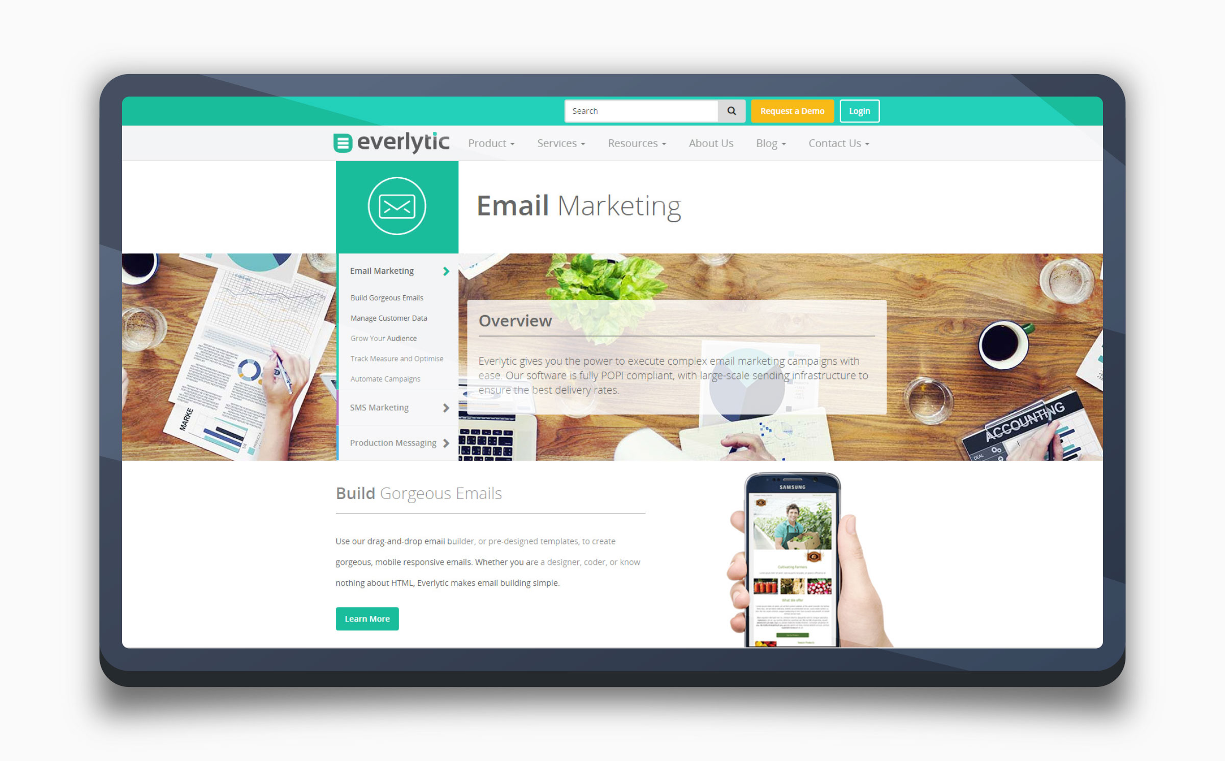 The 2015 Everlytic website on a tablet — a teal header, envelope icon, and a busy wooden-desk stock photo behind the Email Marketing overview